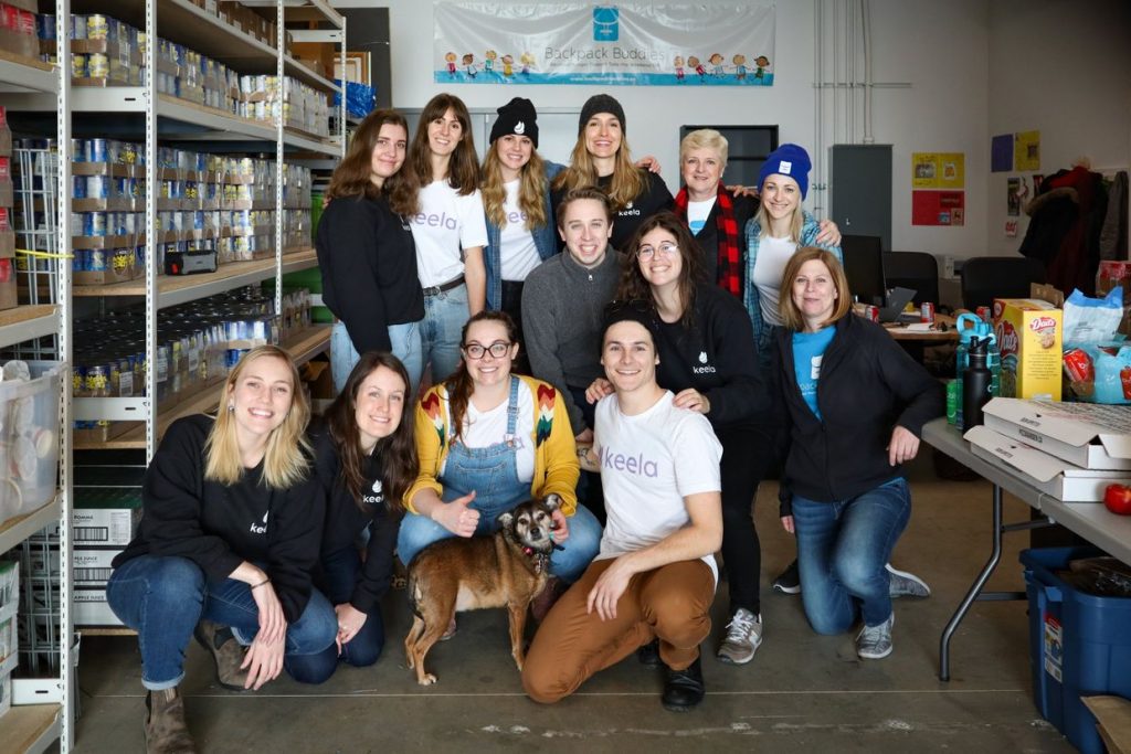 The Keela team and Backpack Buddies staff huddle together for a group photo in their warehouse and office.