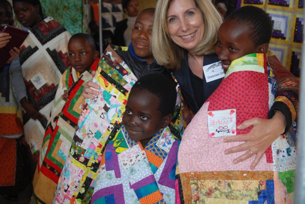 President of the Love Quilt Project poses with children wrapped in quilts
