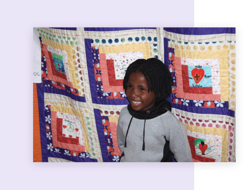 A child standing in front of a quilt hung on a wall