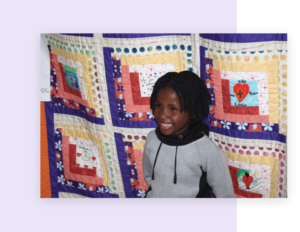 A child standing in front of a quilt hung on a wall