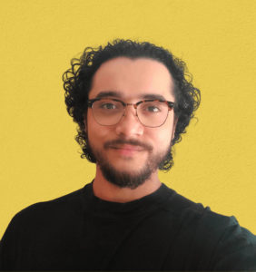 headshot of Travis in a black shirt on a yellow background